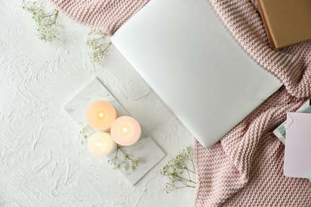 Burning candles, flowers and laptop on table