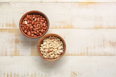 Bowls with peanuts on white wooden background