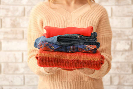 Woman with stack of warm clothes on brick backgroundの写真素材