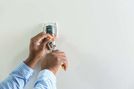 African-American electrician installing switch in room