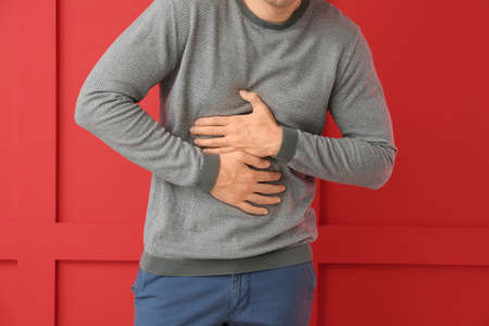 Young man suffering from abdominal pain on color backgroundの写真素材