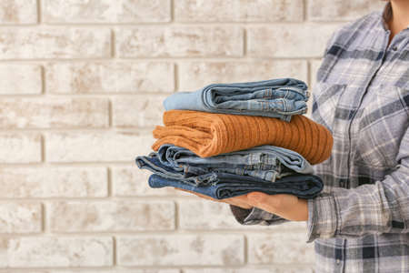 Woman with stack of warm clothes on brick backgroundの写真素材