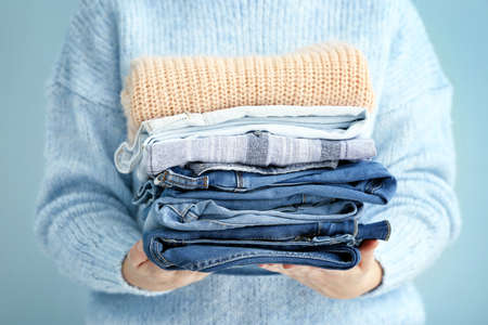 Woman with stack of warm clothes on color background, closeupの写真素材