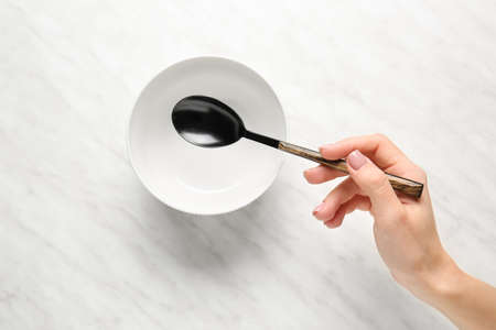 Female hand with spoon and empty bowl on light backgroundの写真素材