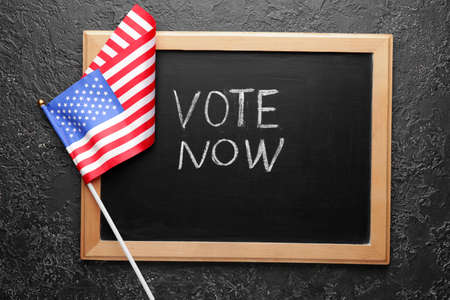 Chalkboard with text VOTE NOW and USA flag on dark backgroundの写真素材