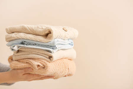 Woman with stack of warm clothes on color backgroundの写真素材