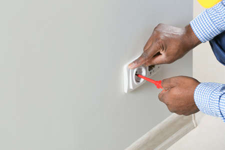 African-American electrician replacing socket in roomの写真素材
