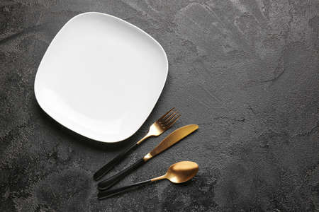 Empty plate and cutlery on dark background