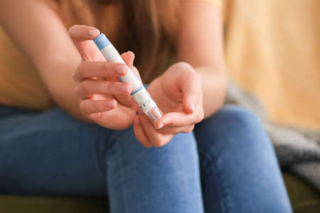 Diabetic woman taking blood sample with lancet pen at home, closeupの写真素材