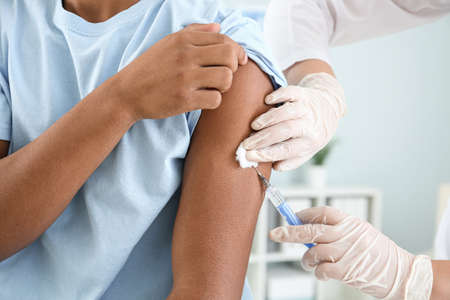 Doctor vaccinating teenage boy in clinic, closeup