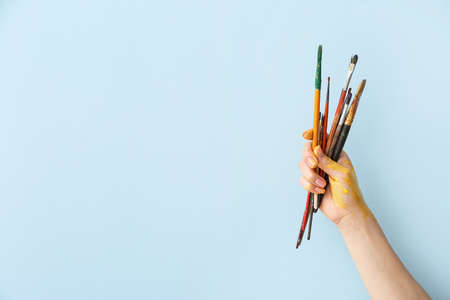 Hand of artist with brushes on color backgroundの写真素材