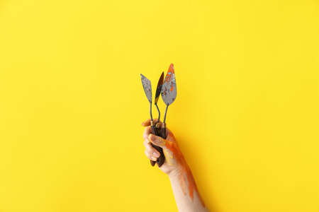 Hand of artist with palette knives on color backgroundの写真素材