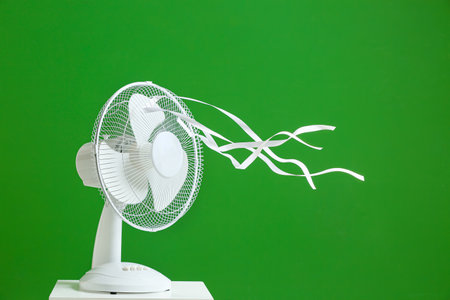 Electric fan with fluttering ribbons on color background