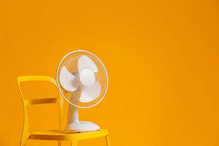 Electric fan on chair against color backgroundの写真素材