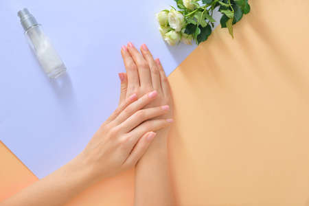 Hands of young woman and bottle of cream with flowers on color backgroundの写真素材