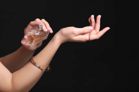 Hands of beautiful young woman with bottle of perfume on dark backgroundの写真素材