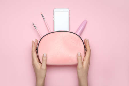 Female hands with cosmetic bag and mobile phone on color backgroundの写真素材