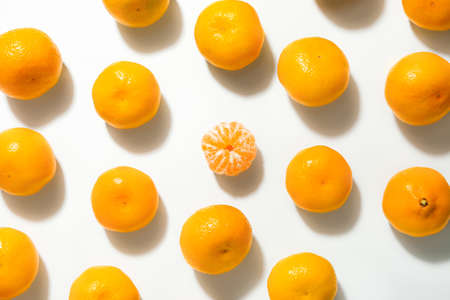Peeled tangerine among unpeeled ones on white background. Concept of uniquenessの写真素材