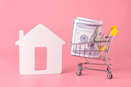 Figure of house and money in shopping cart on color background. Concept of buying real estateの写真素材