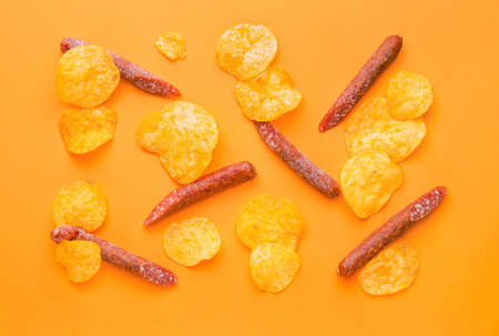 Tasty potato chips and smoked sausages on color backgroundの写真素材
