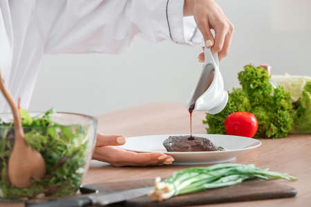 Female chef adding sauce to tasty meat in kitchen