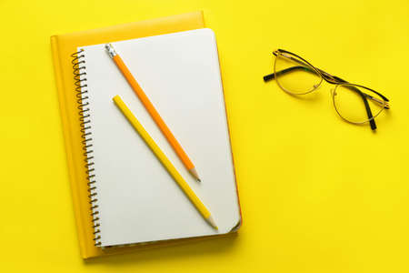 Stylish notebooks with pencils and eyeglasses on color background