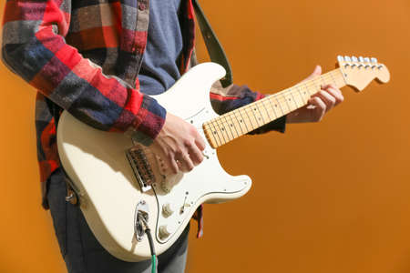 Young man playing guitar on color background