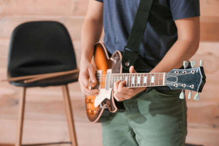 Young man playing guitar near wooden wallの写真素材