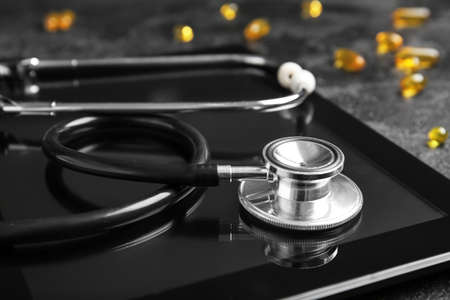 Stethoscope, tablet computer and pills on dark background, closeup