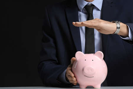 Male bank manager with piggy bank sitting at table against dark backgroundの写真素材