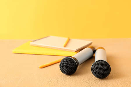 Microphones and notebooks on table against color background