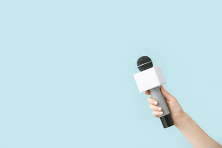Journalist's hand with microphone on color background