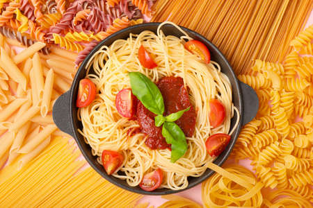 Frying pan with boiled, raw pasta and tomato sauce on color backgroundの写真素材