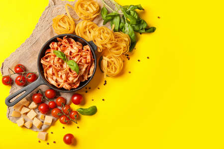 Frying pan with boiled, raw pasta and tomato sauce on color backgroundの写真素材