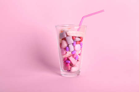 Glass with different chewing gums on color background