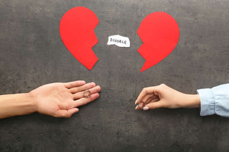 Hands of couple with broken heart and wedding rings on dark background. Concept of divorce