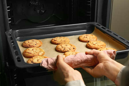 Woman taking baking tray with cookies out of oven