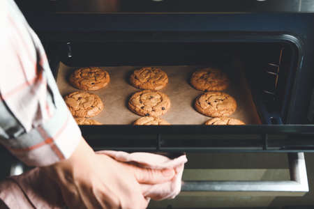 Woman taking baking tray with cookies out of ovenの写真素材