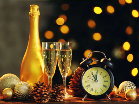 Alarm clock with Christmas decor and champagne on table against defocused lights