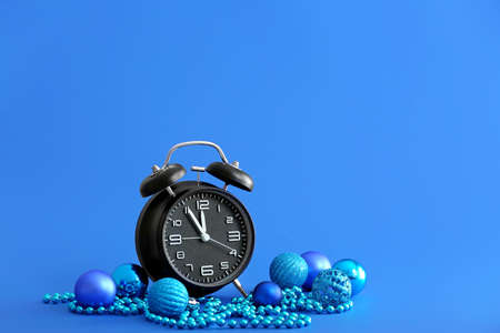 Alarm clock with Christmas decor on color background