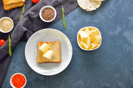 Bowl with fresh butter and bread on dark background