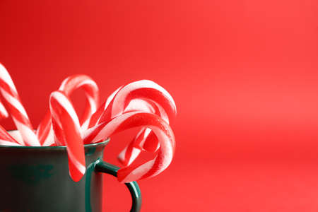 Mug with Christmas candy canes on color background, closeup