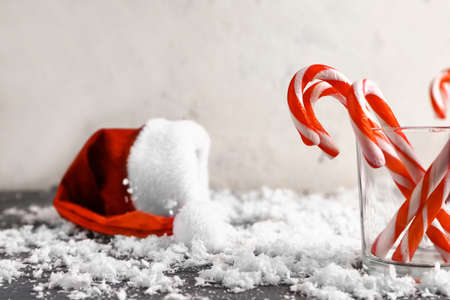 Glass with Christmas candy canes, Santa hat and snow on tableの写真素材