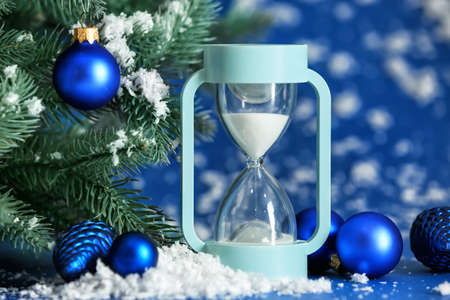 Hourglass, snow and fir tree on color background. Christmas countdown concept