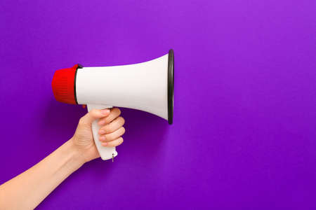 Female hand with megaphone on color background