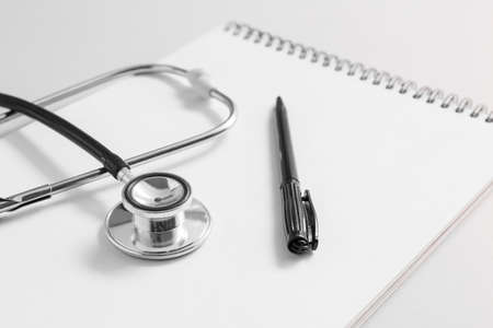 Stethoscope, notebook and pen on light background, closeup. Cardiology concept