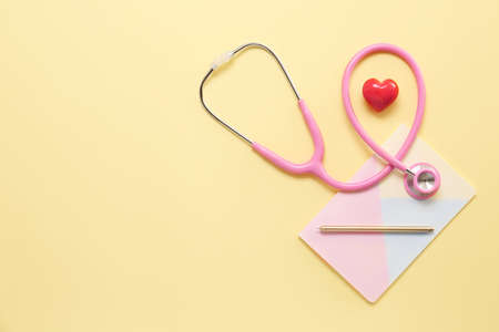 Stethoscope, heart and notebook on color background. Cardiology concept