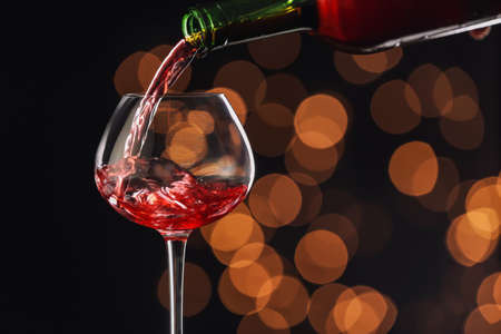 Pouring of wine into glass on dark background with blurred lightsの写真素材