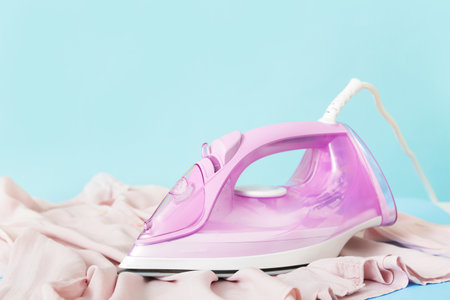 Electric iron with clean clothes on color backgroundの写真素材