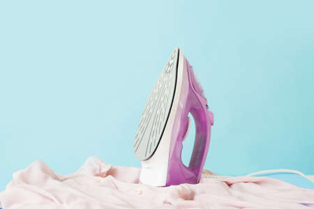 Electric iron with clean clothes on color backgroundの写真素材